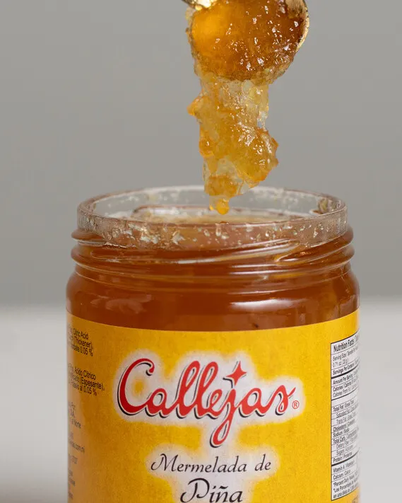 Mermelada de piña Callejas con una cucharada de dulce cayendo sobre el frasco.