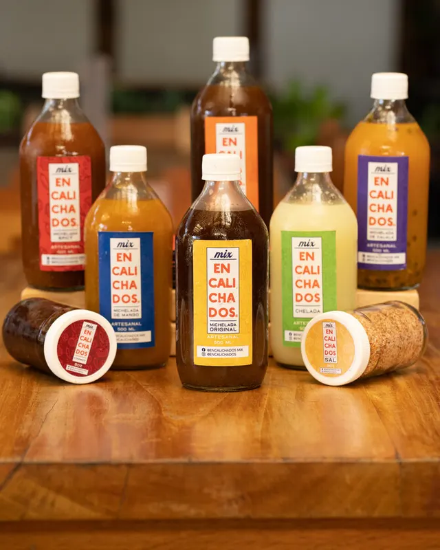 Botellas de micheladas artesanales Encalichados de varios sabores sobre una mesa de madera.