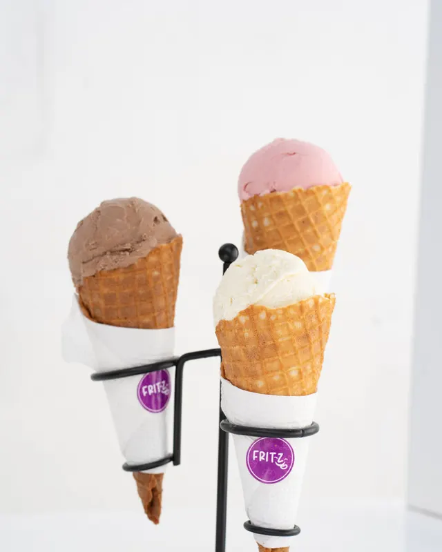 Tres conos de helado de sabores distintos en un soporte, con el sello morado de Fritz.