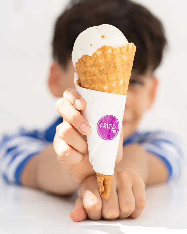 Un niño sostiene un cono de helado envuelto en servilleta con el sello de Fritz.