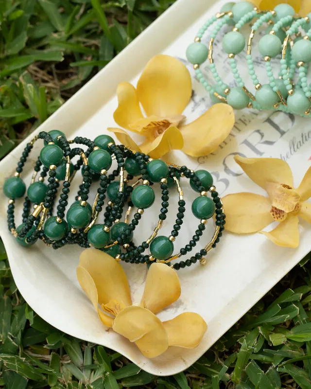 Pulseras de cuentas verdes y turquesa sobre una bandeja con orquídeas amarillas, en el pasto, de Iconika.