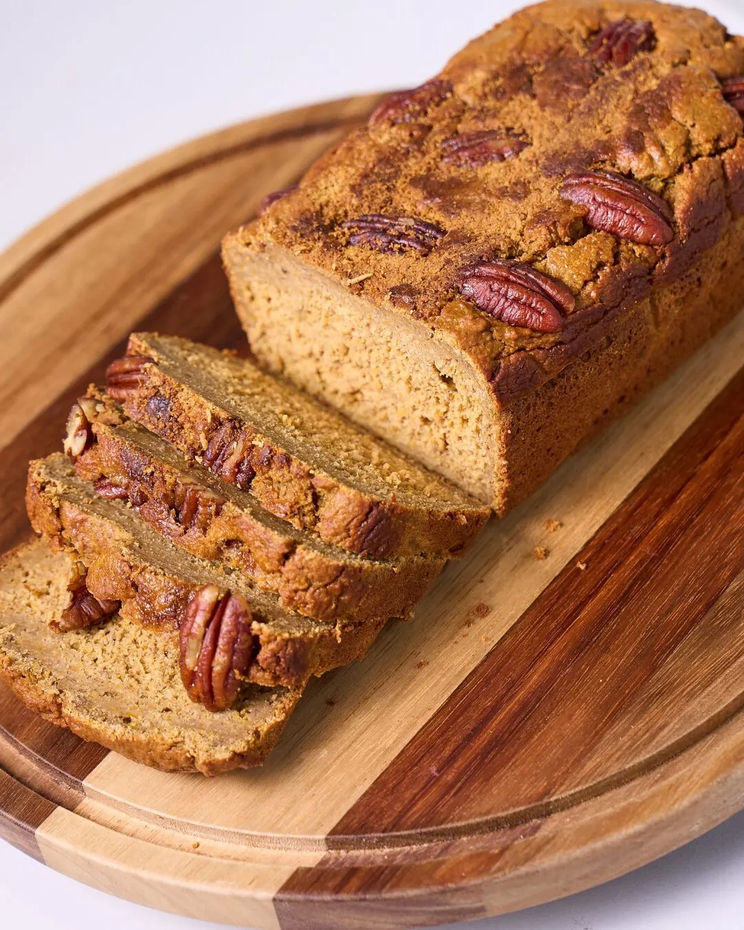 A sliced loaf with pecans on a wooden board.