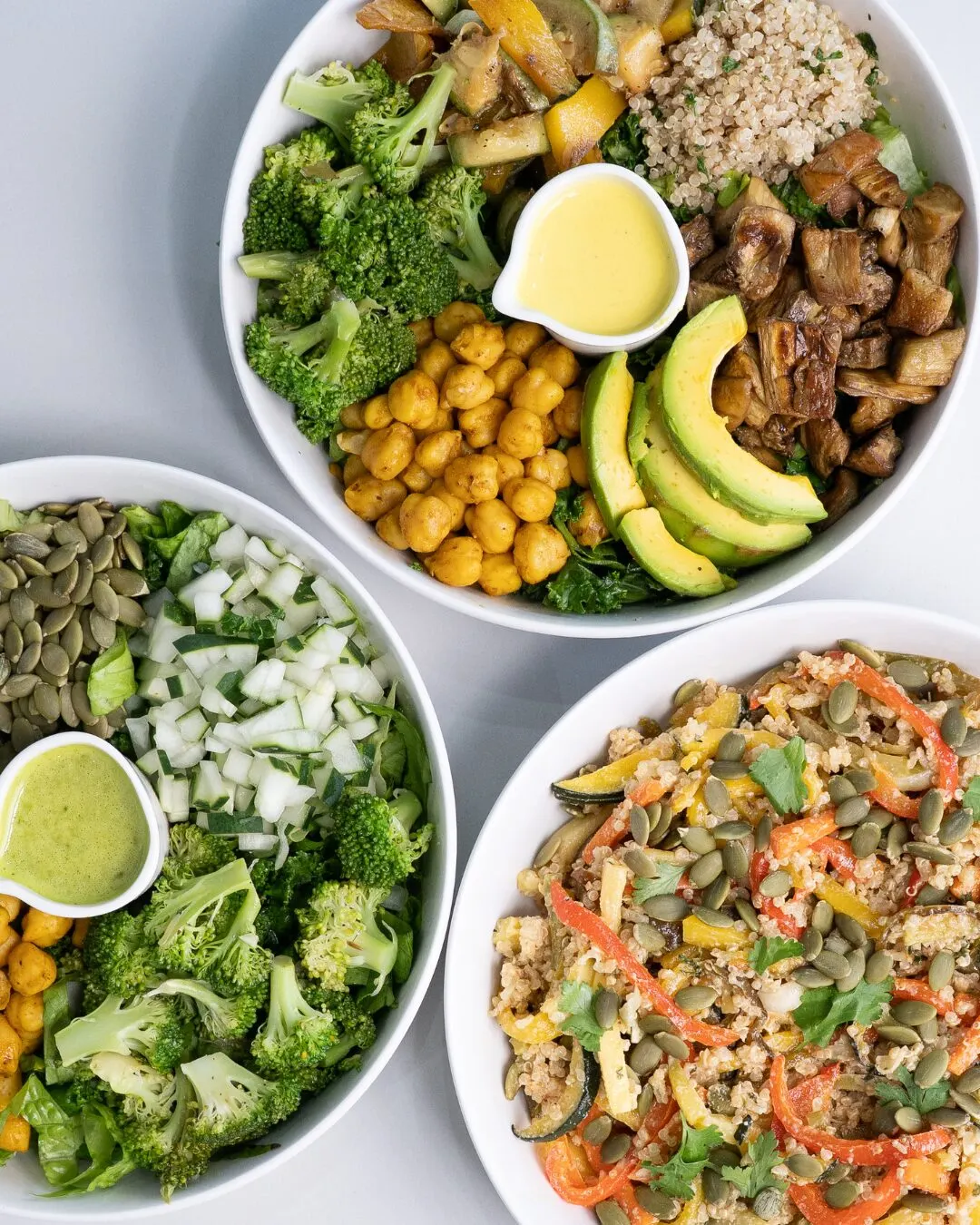 Three bowls seen from above, with broccoli, chickpeas, avocado, mushrooms and a green sauce.