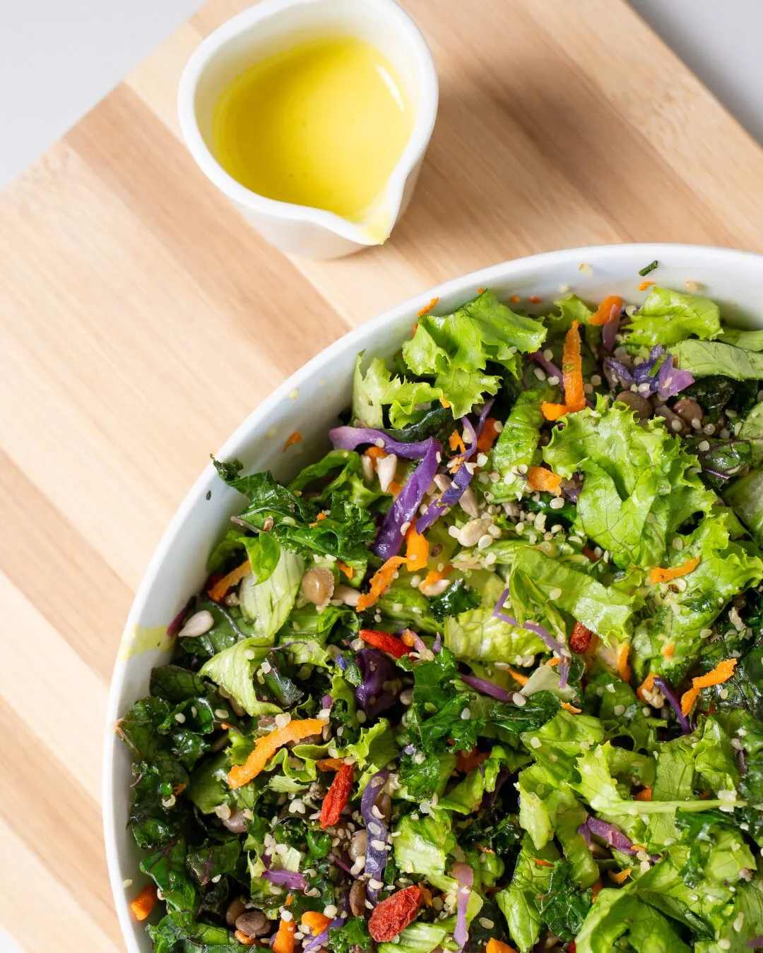 A white bowl of chopped salad with lettuce, carrot and purple cabbage, beside a jug of oil.
