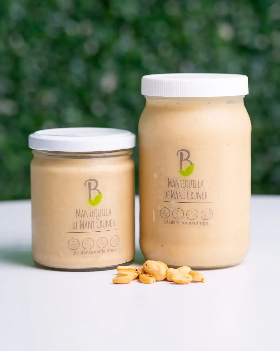 Two jars of nut butter with white lids and a few nuts in front, against a green background.
