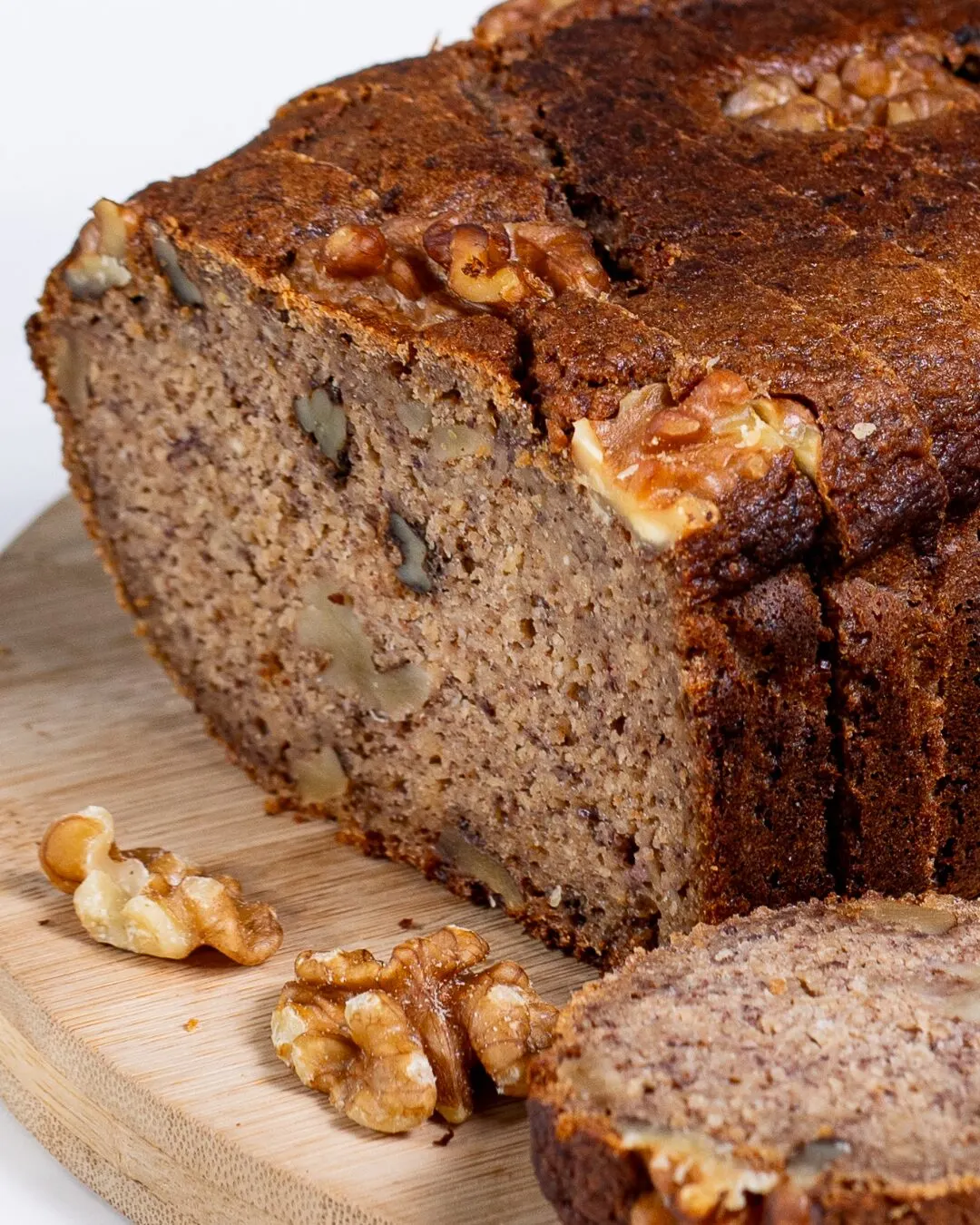 A sliced walnut loaf with whole walnuts on a wooden board.