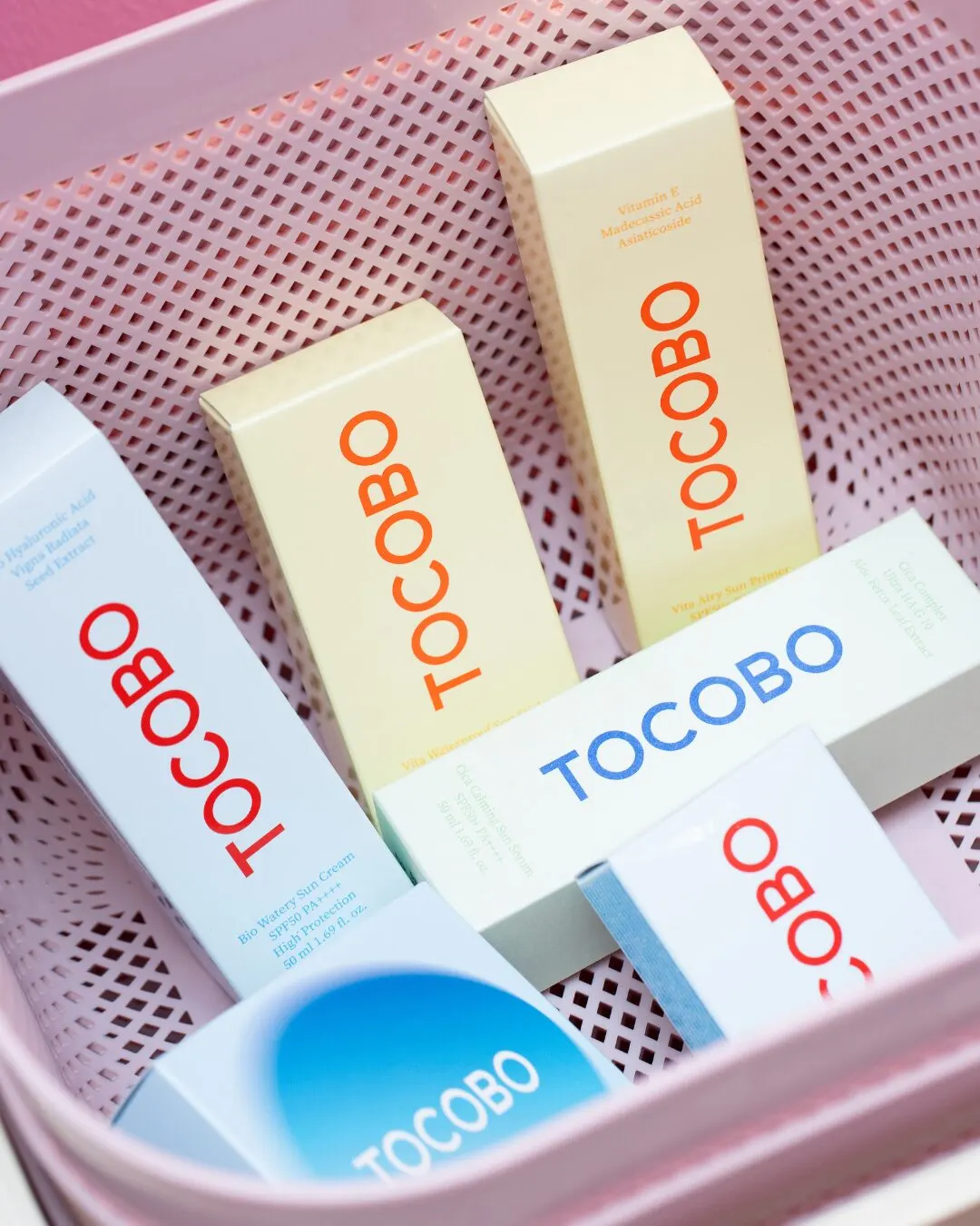 A pink basket with boxes of skincare products in yellow and blue.