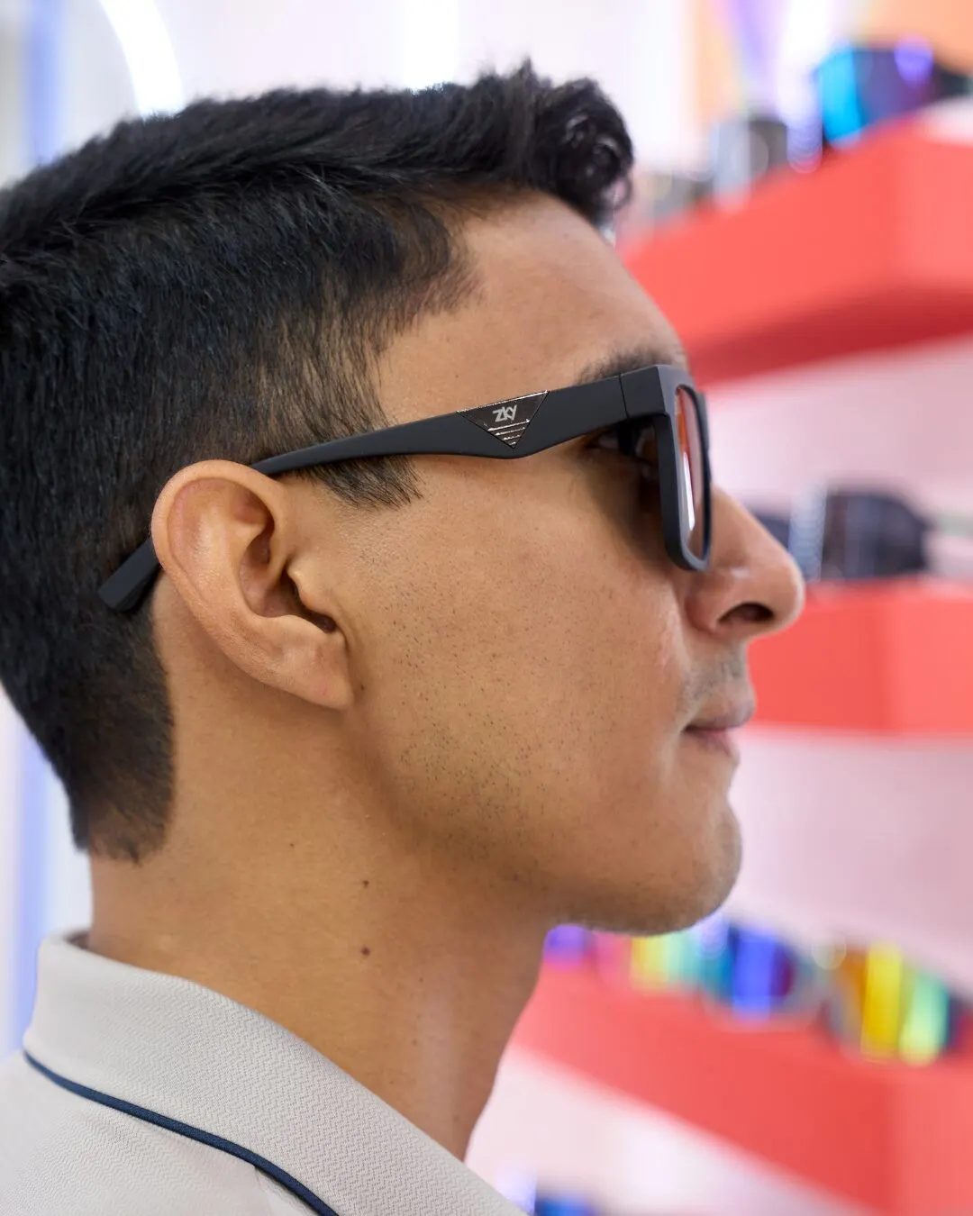 Profile of a man in dark sunglasses in front of shelves of colored sunglasses.