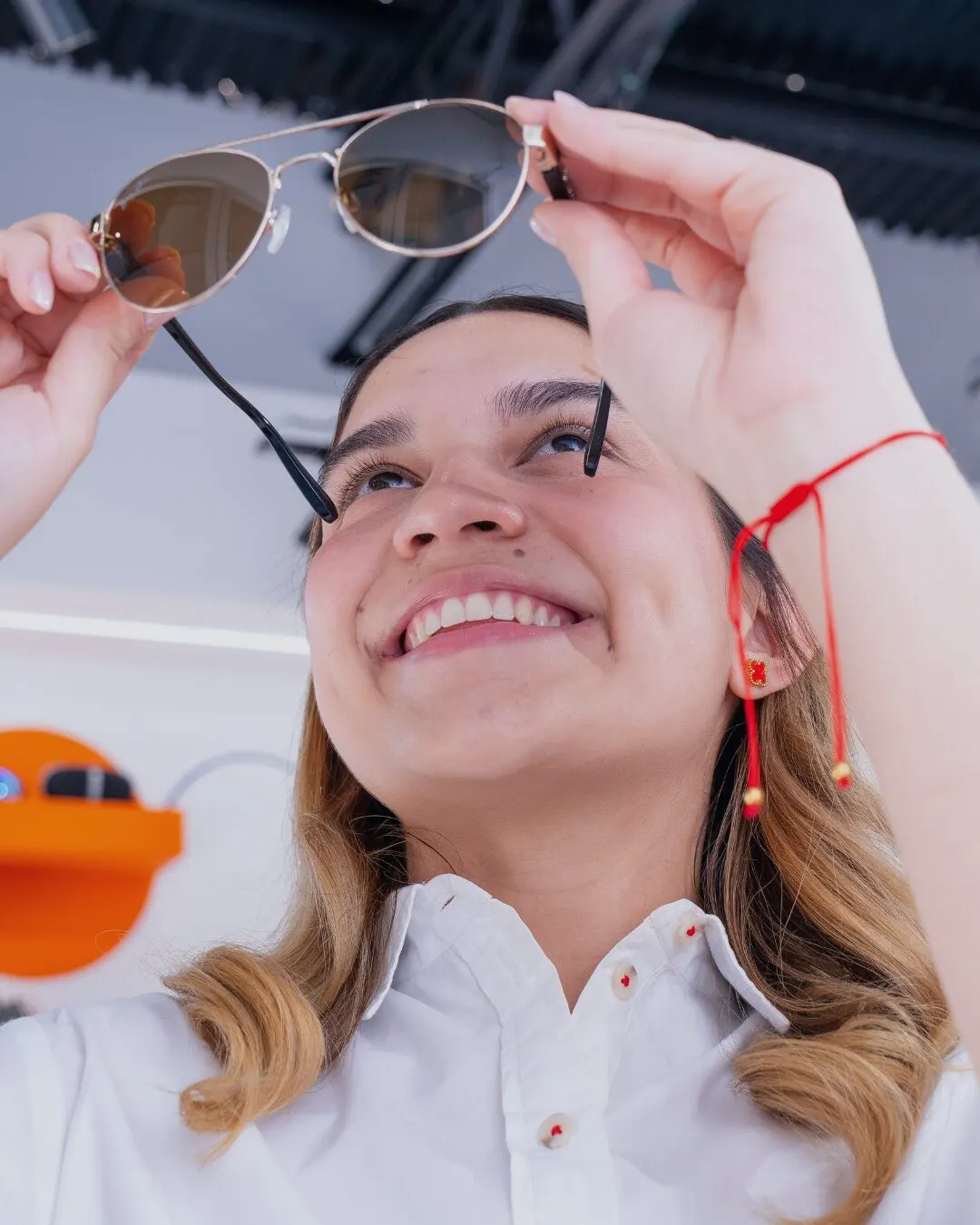 A smiling woman holding sunglasses with a red cord above her face.