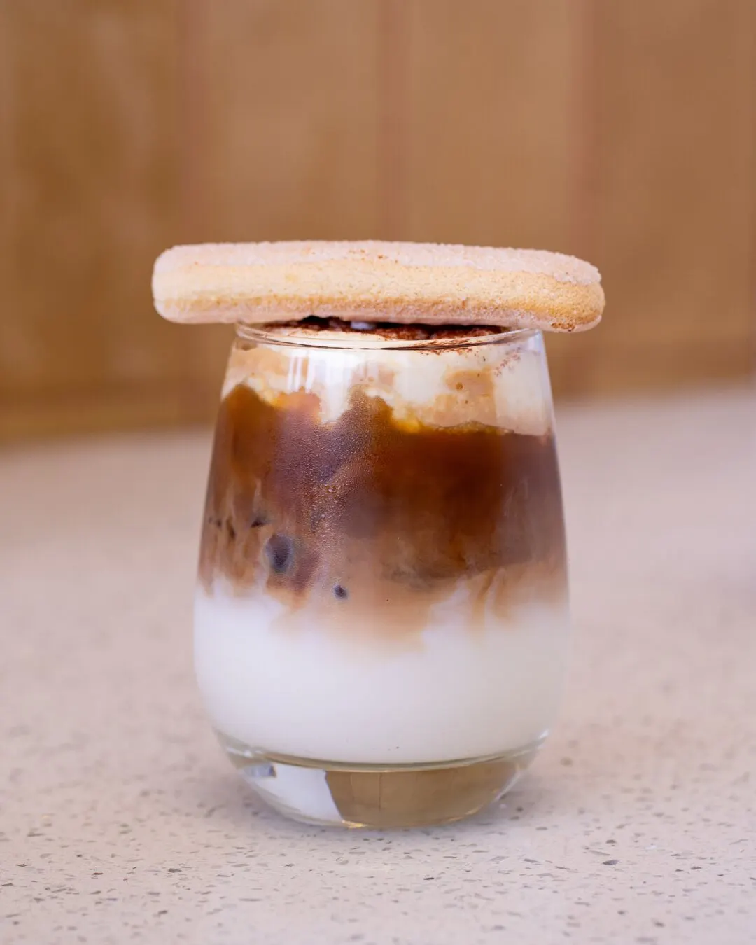 Café con leche helado en vaso de vidrio con una galleta encima.