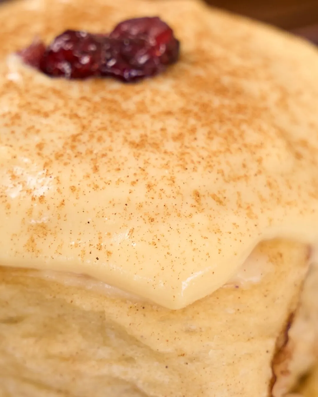 Detalle de un pastel cubierto de crema pastelera con canela y un toque de mermelada roja.