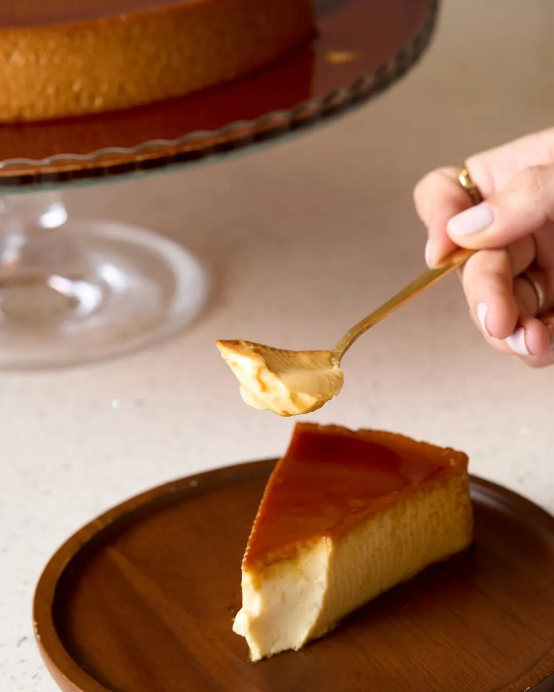 Cucharada de crema sobre una porción de flan con caramelo, en un plato de madera.