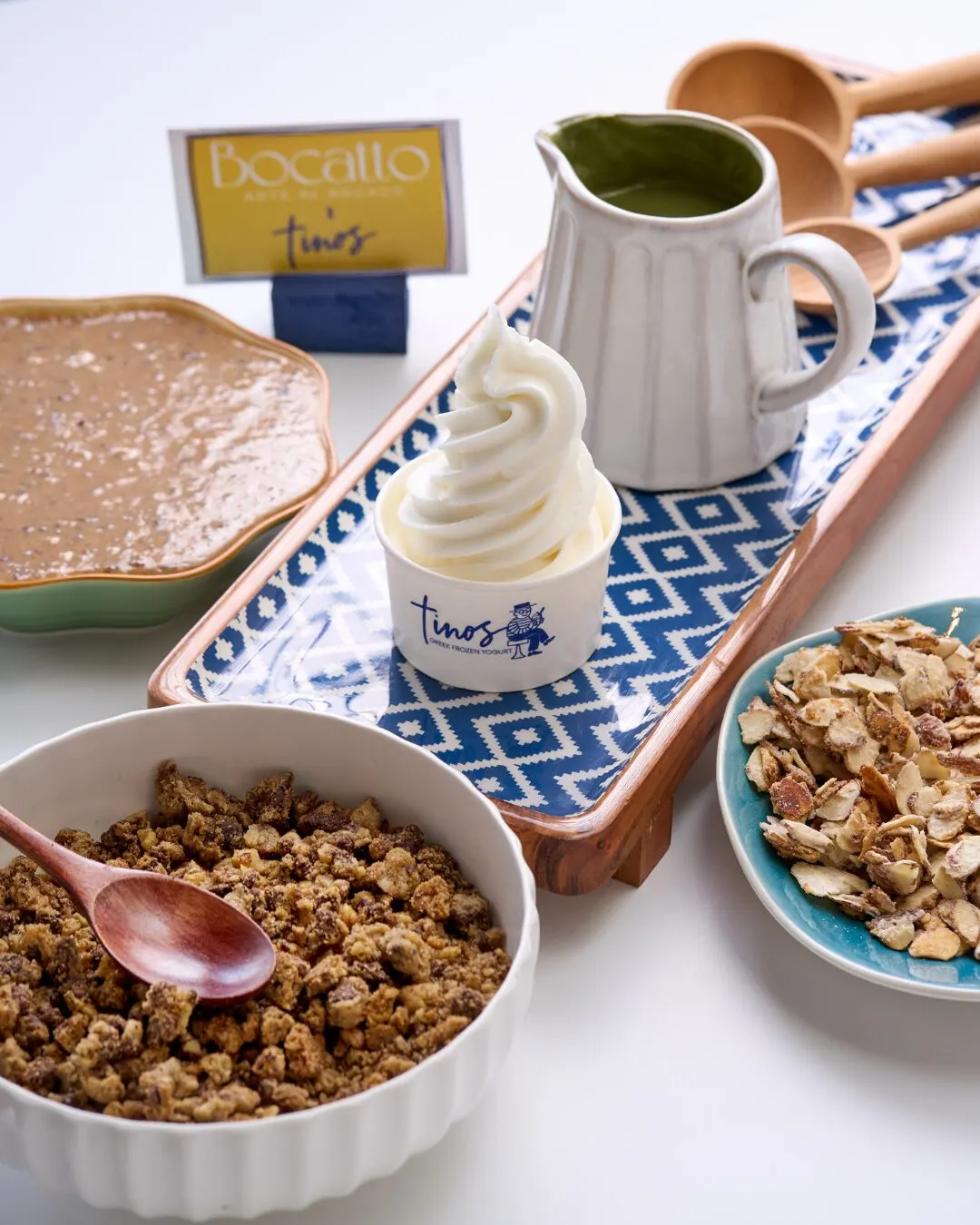 Granola, un helado suave en vaso de Tino's y una jarra de matcha sobre una bandeja azul, con el letrero de Bocatto x Tino's.