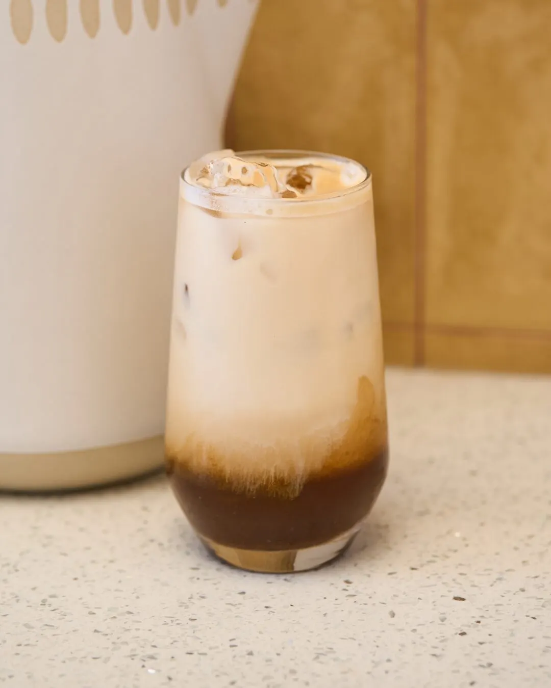 Vaso de café helado con leche sobre una encimera clara.