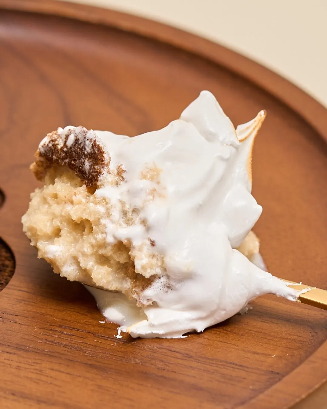 Porción de pastel con merengue levantada con una cuchara sobre un plato de madera.