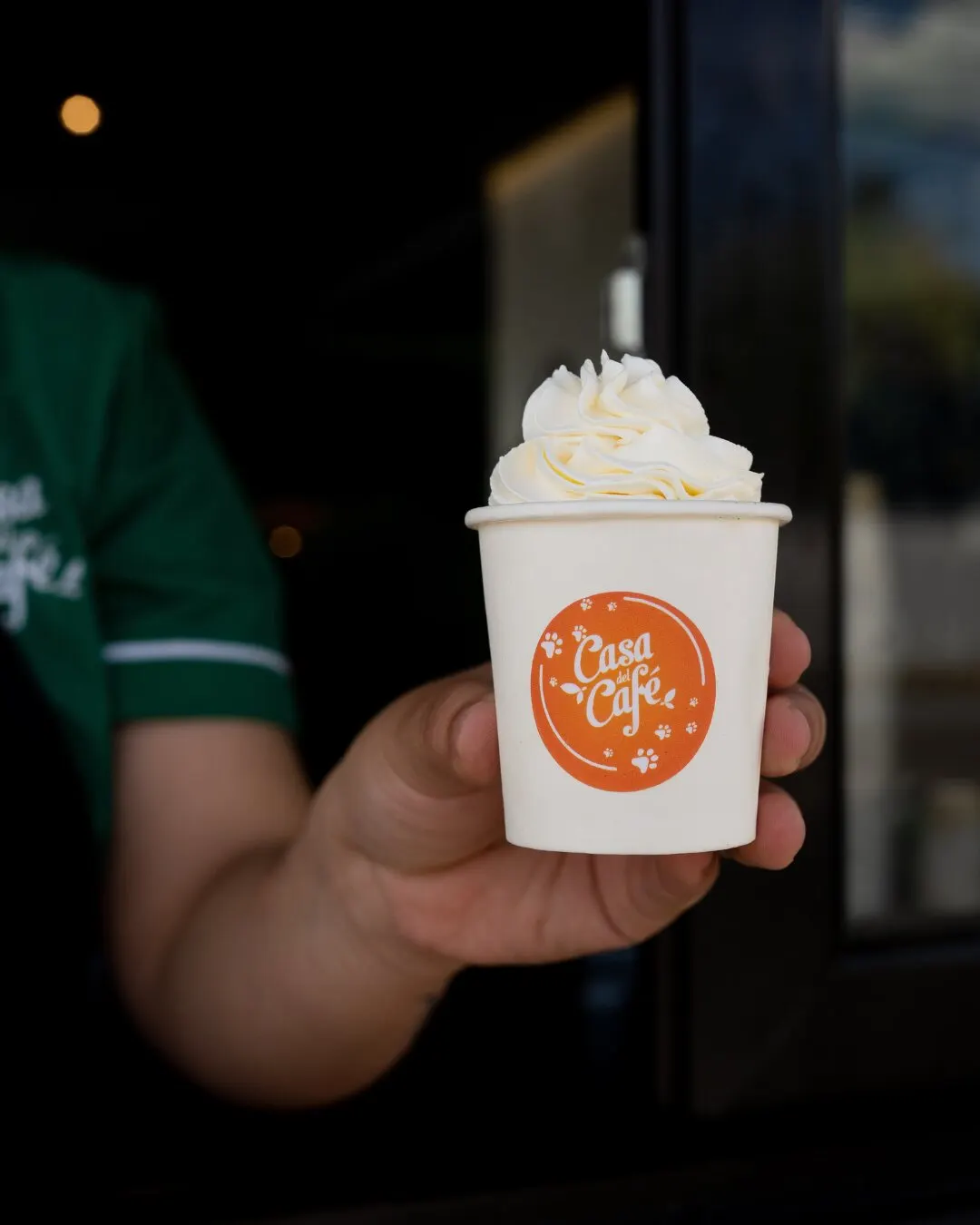 Mano sosteniendo una bebida con crema batida en un vaso de Casa del Café.