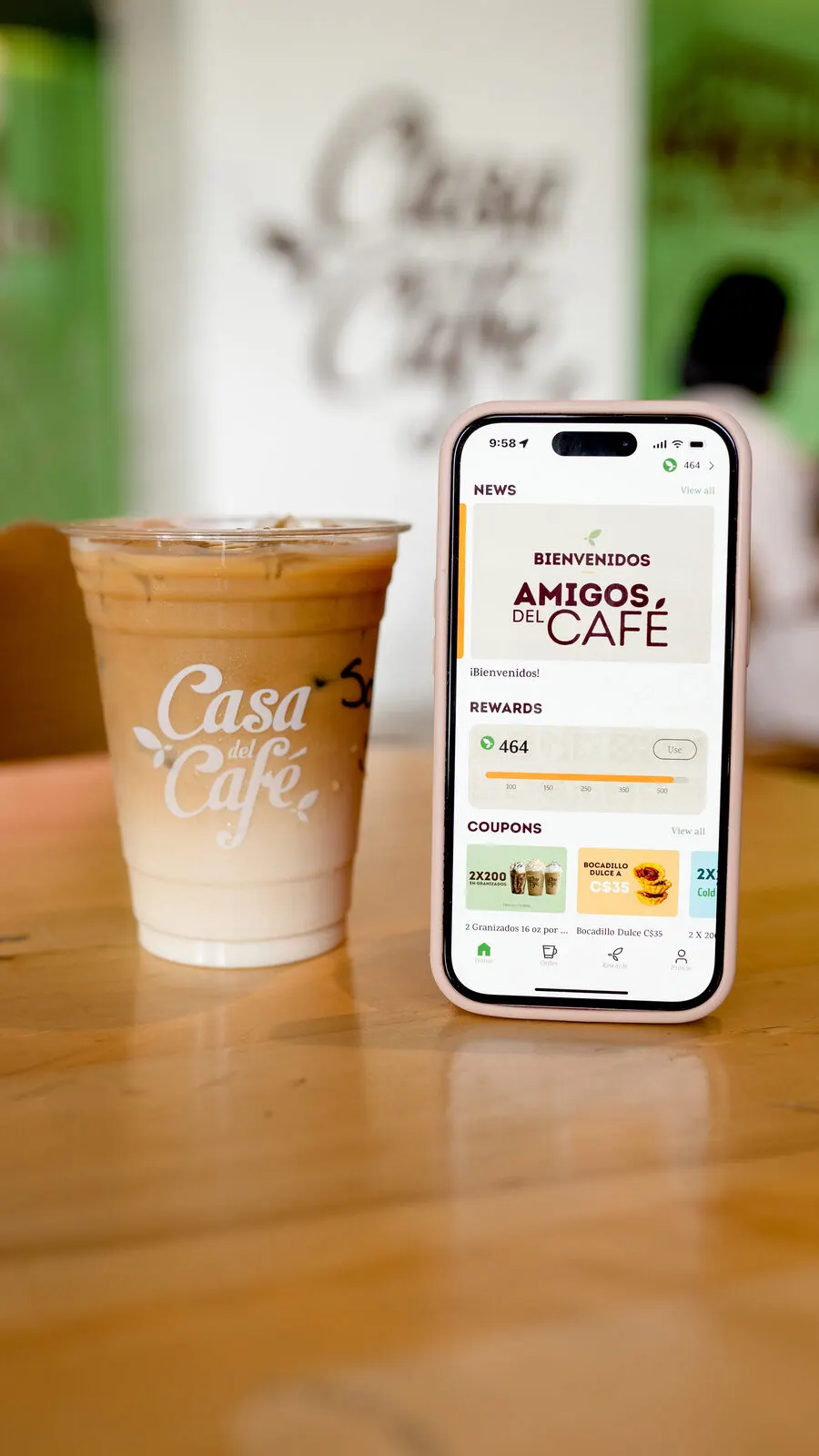 Café helado y un celular con la app de Casa del Café sobre una mesa de madera.