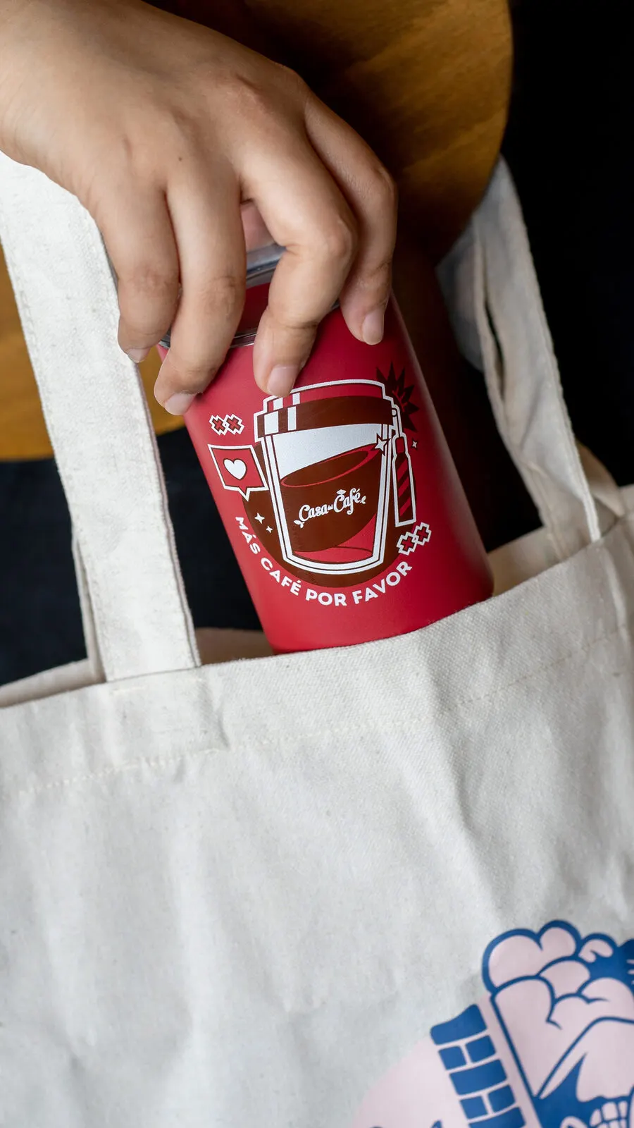 Mano sacando un vaso rojo de Casa del Café de una bolsa de tela.