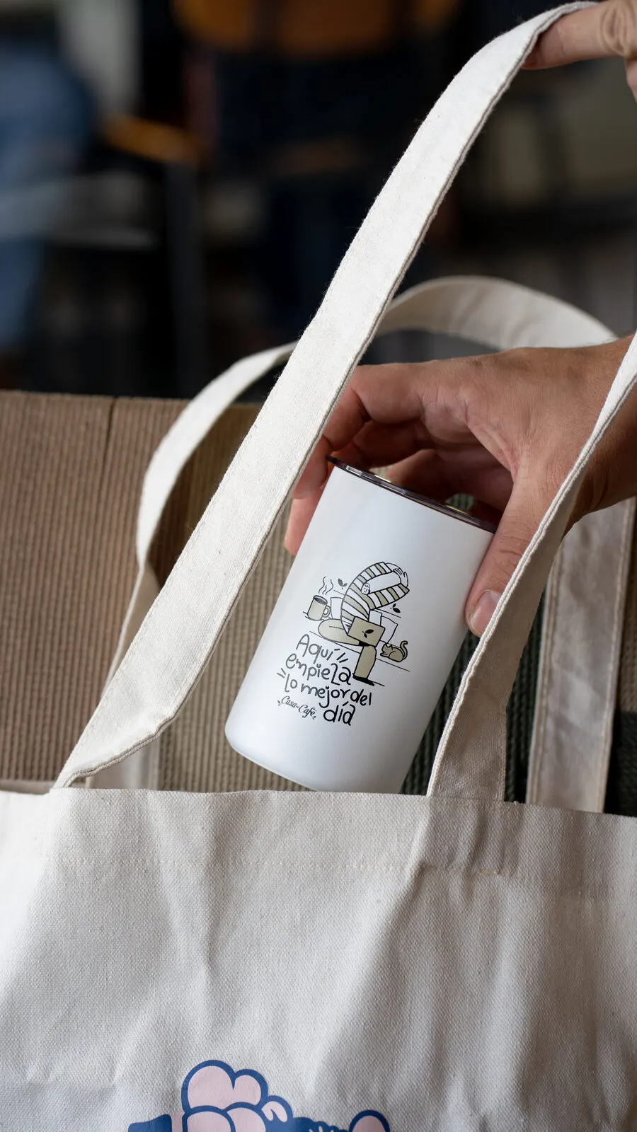 Mano sacando un termo blanco de una bolsa de tela.