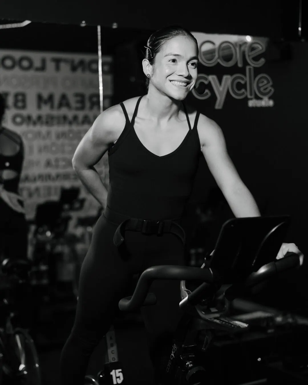 Instructora sonriente junto a una bicicleta, en blanco y negro.