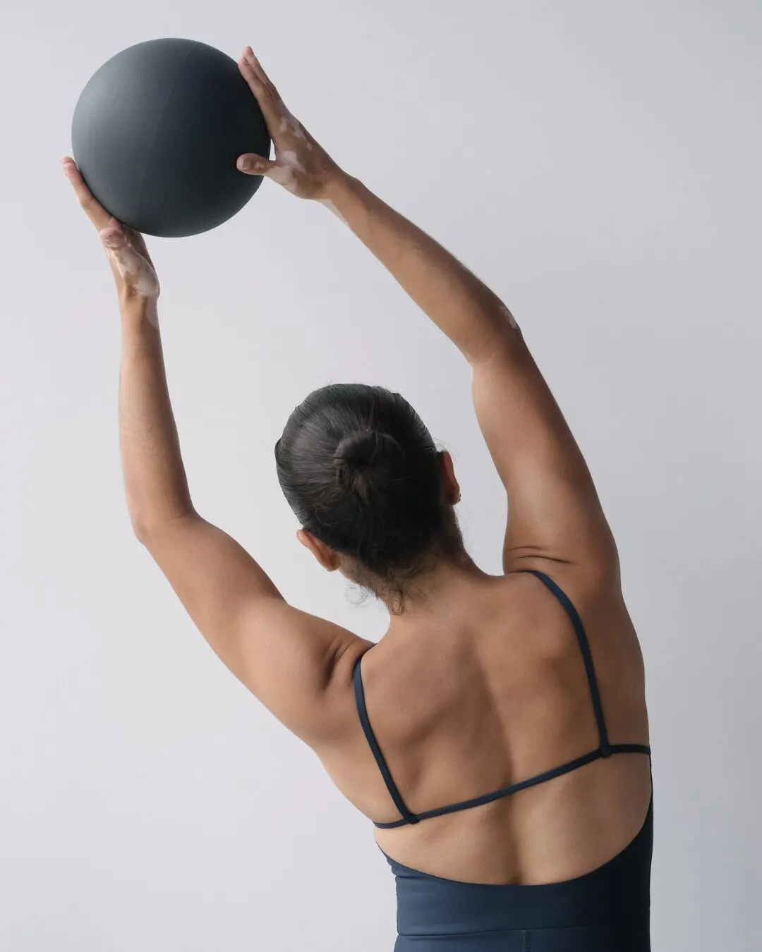 Mujer de espaldas levantando una pelota con los brazos estirados.