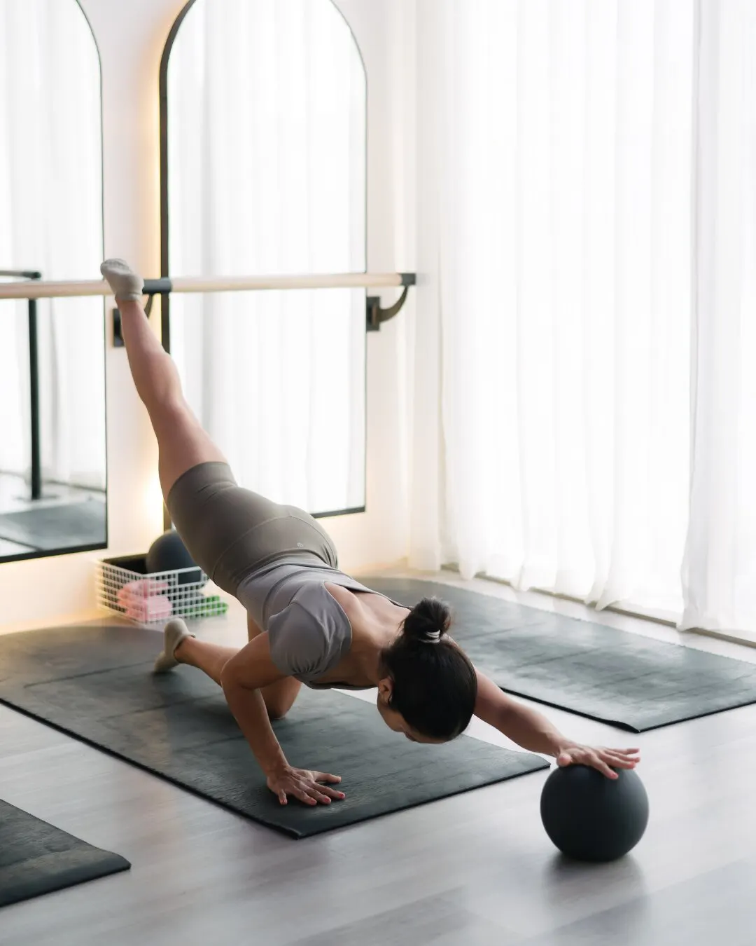 Mujer en plancha con un pie sobre una pelota, junto a la ventana del estudio.