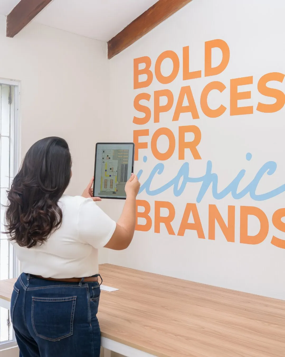 Mujer con una tablet frente a una pared con el texto Bold spaces for iconic brands.