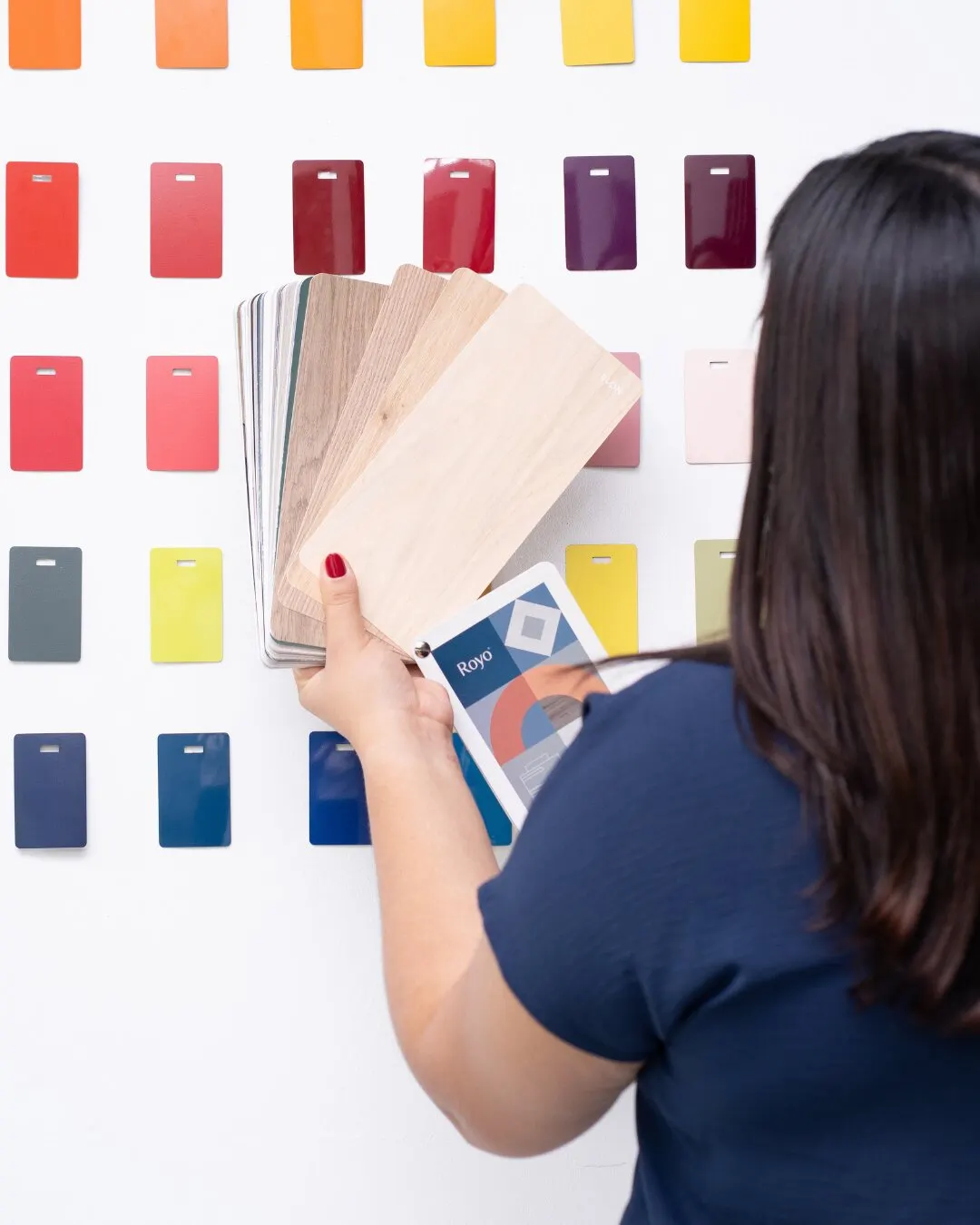 Mujer revisando muestrarios de madera frente a una pared de muestras de color.