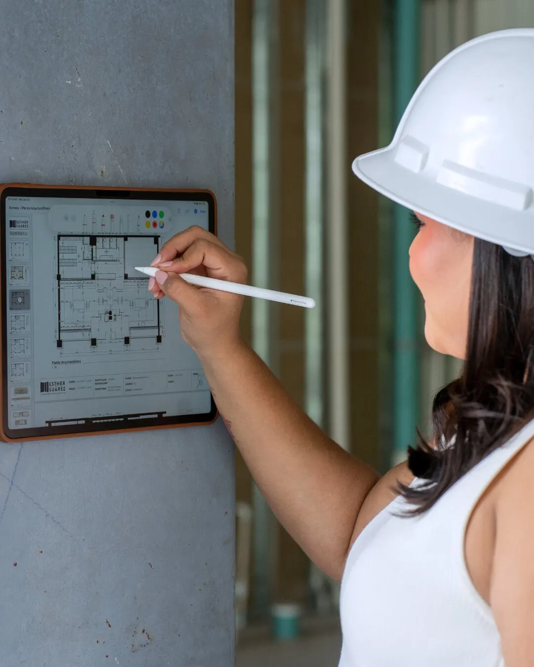 Mujer con casco blanco dibujando un plano en una tablet.
