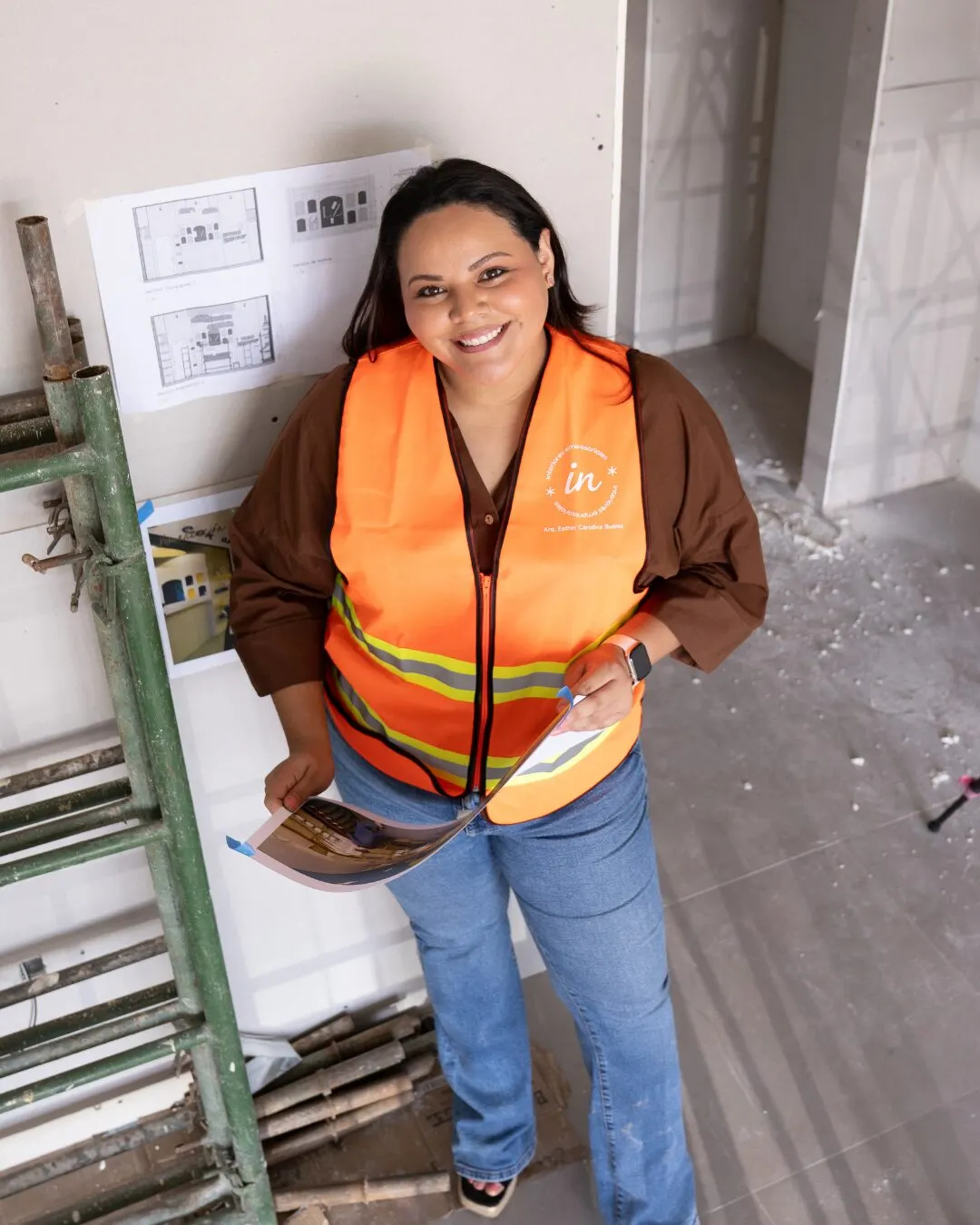 Mujer con chaleco naranja reflectivo en una obra en construcción, con un catálogo en la mano.