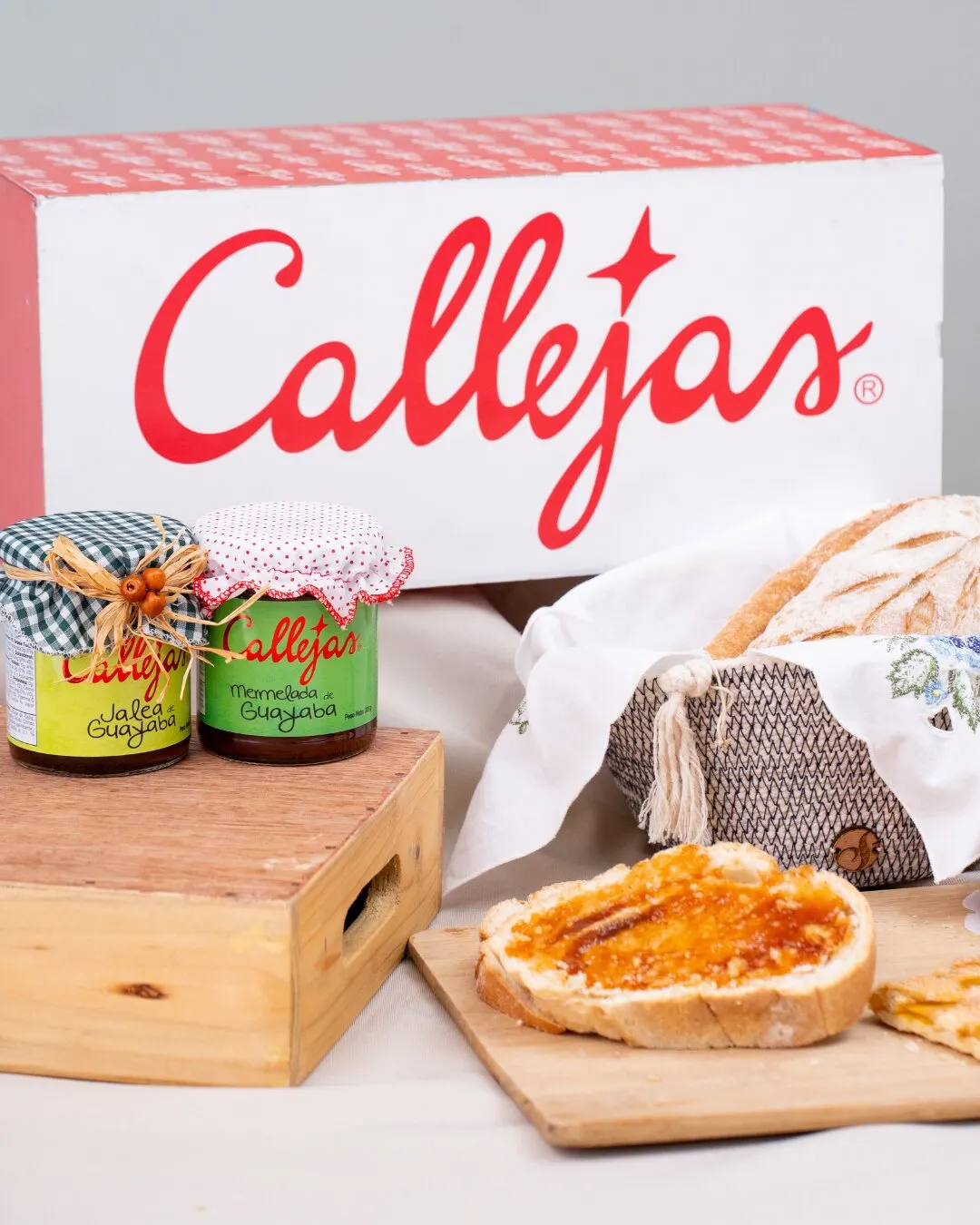 Caja con el logo de Callejas, dos frascos de jalea y una tostada con mermelada sobre una tabla.
