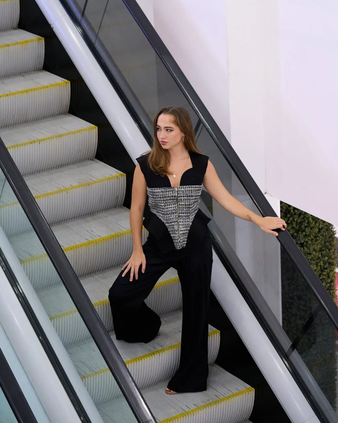 Modelo en unas escaleras eléctricas con un top bordado y pantalón negro de bota ancha.