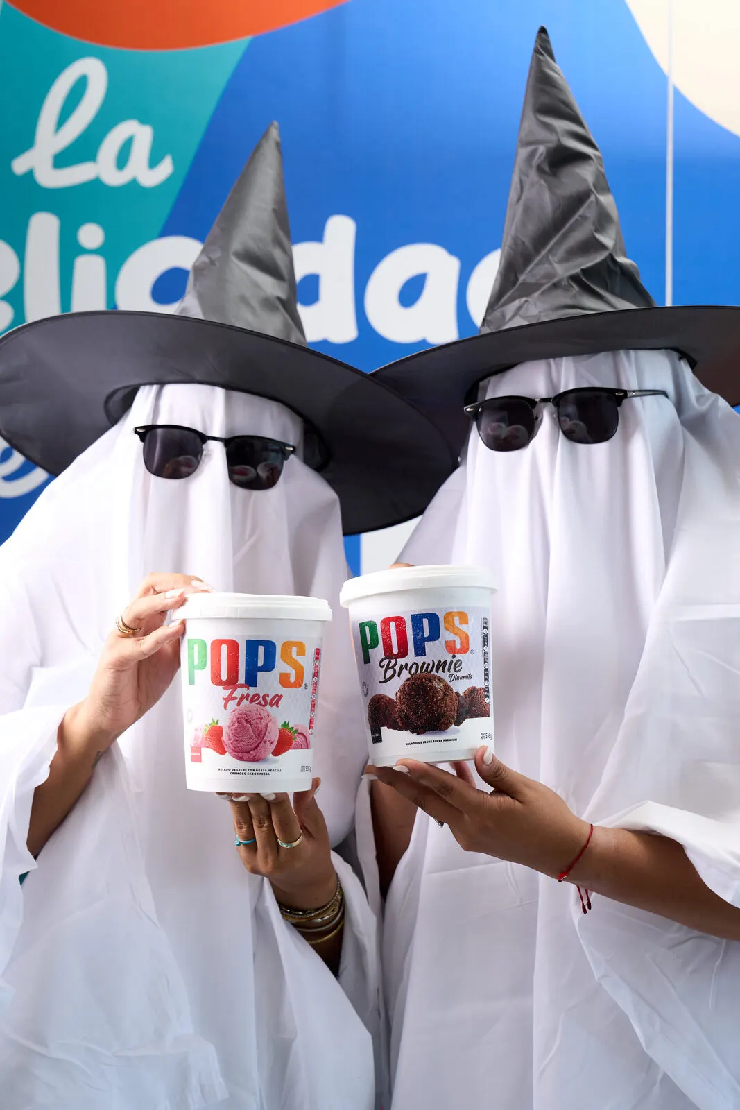 Dos personas disfrazadas de fantasma, con sombreros de bruja y lentes de sol, sosteniendo vasos de helado POPS.