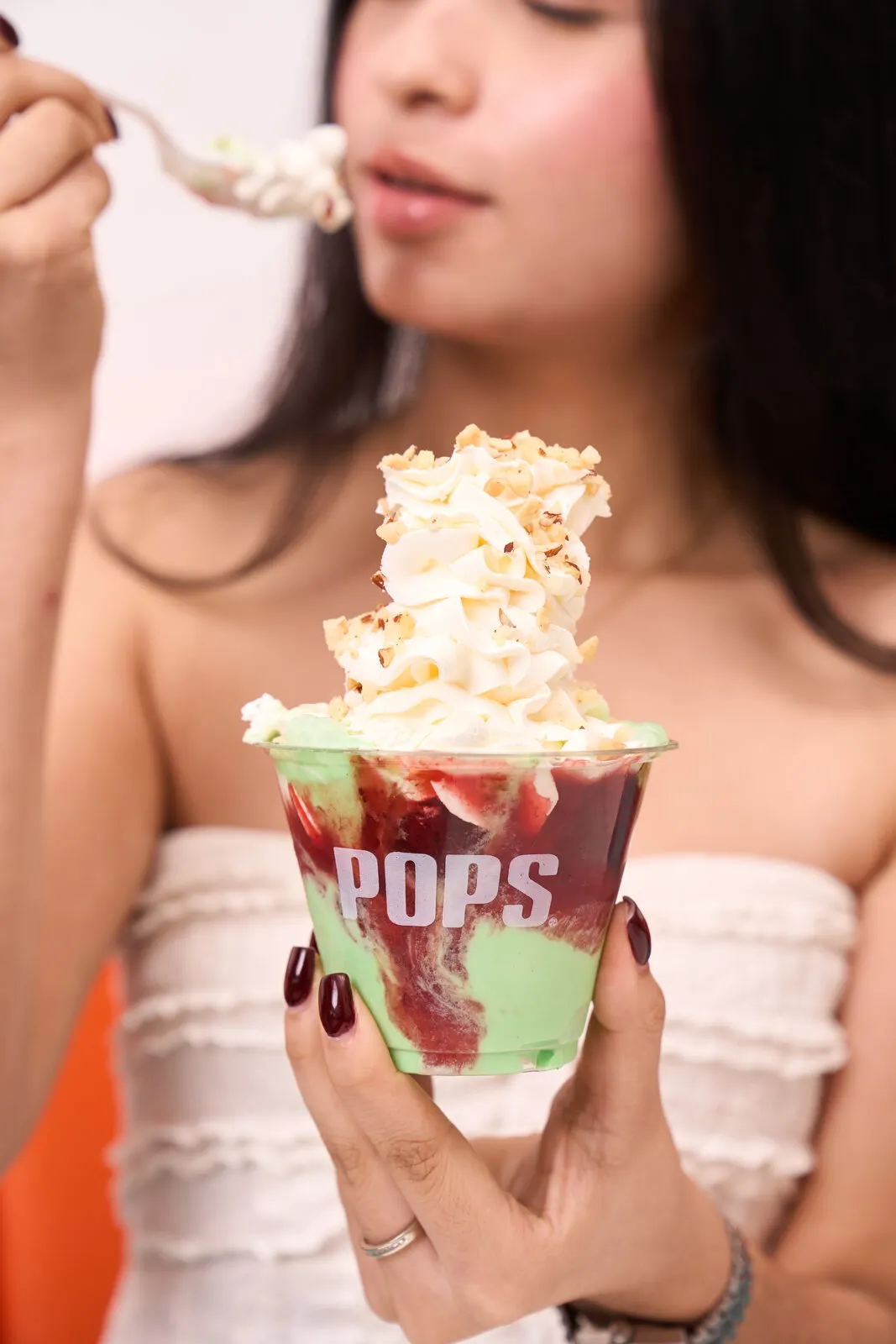Mujer sosteniendo un vaso POPS con helado y crema batida.