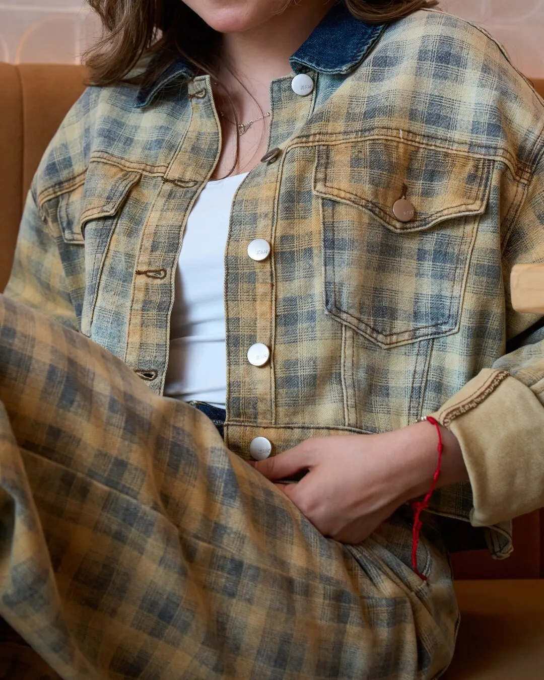 Detalle de una chaqueta de cuadros desgastados con botones blancos, puesta por una modelo sentada.
