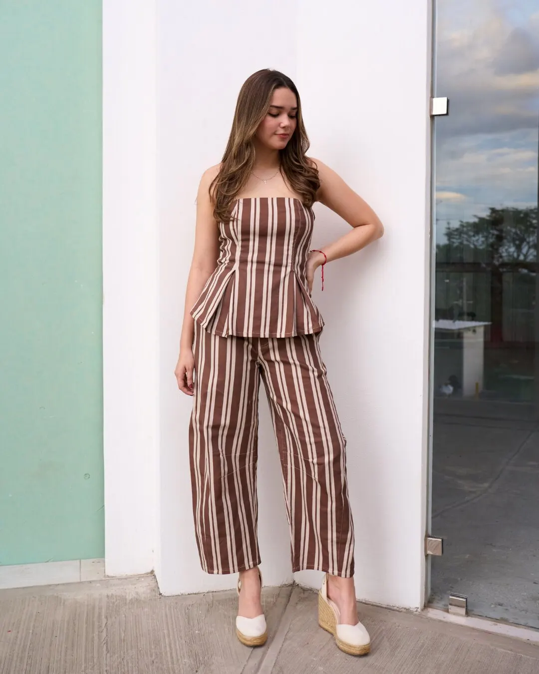 Modelo con top y pantalón ancho de rayas café y crema, y alpargatas, frente a una pared blanca y otra verde menta.