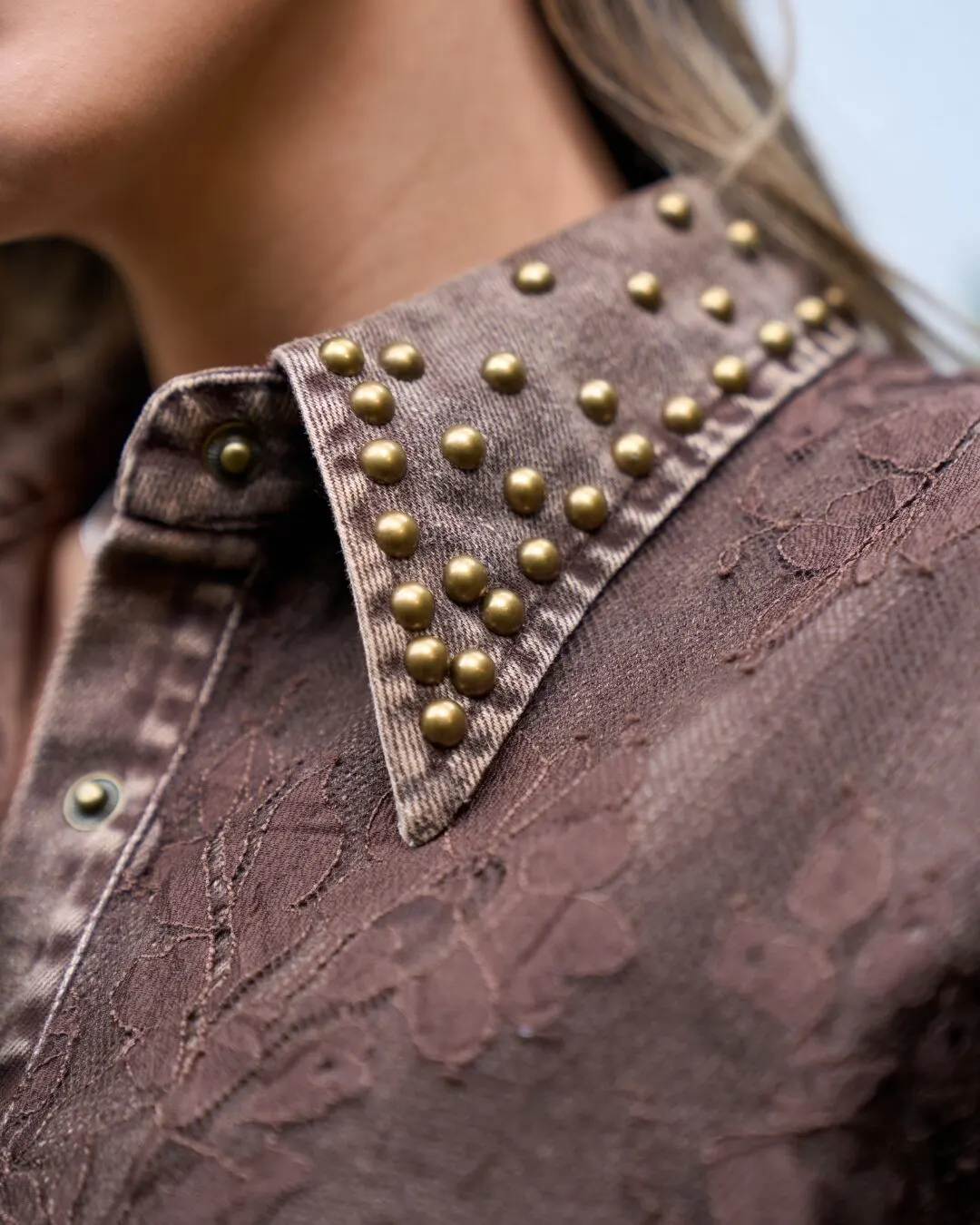 Detalle del cuello de una camisa café con tachuelas doradas.