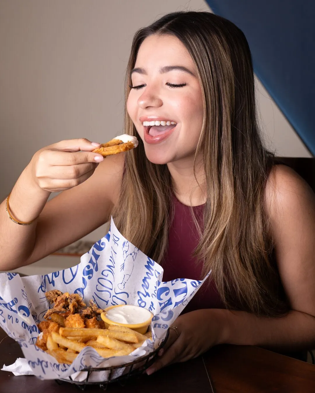 Mujer riendo mientras come de una canasta de fritos con salsa.