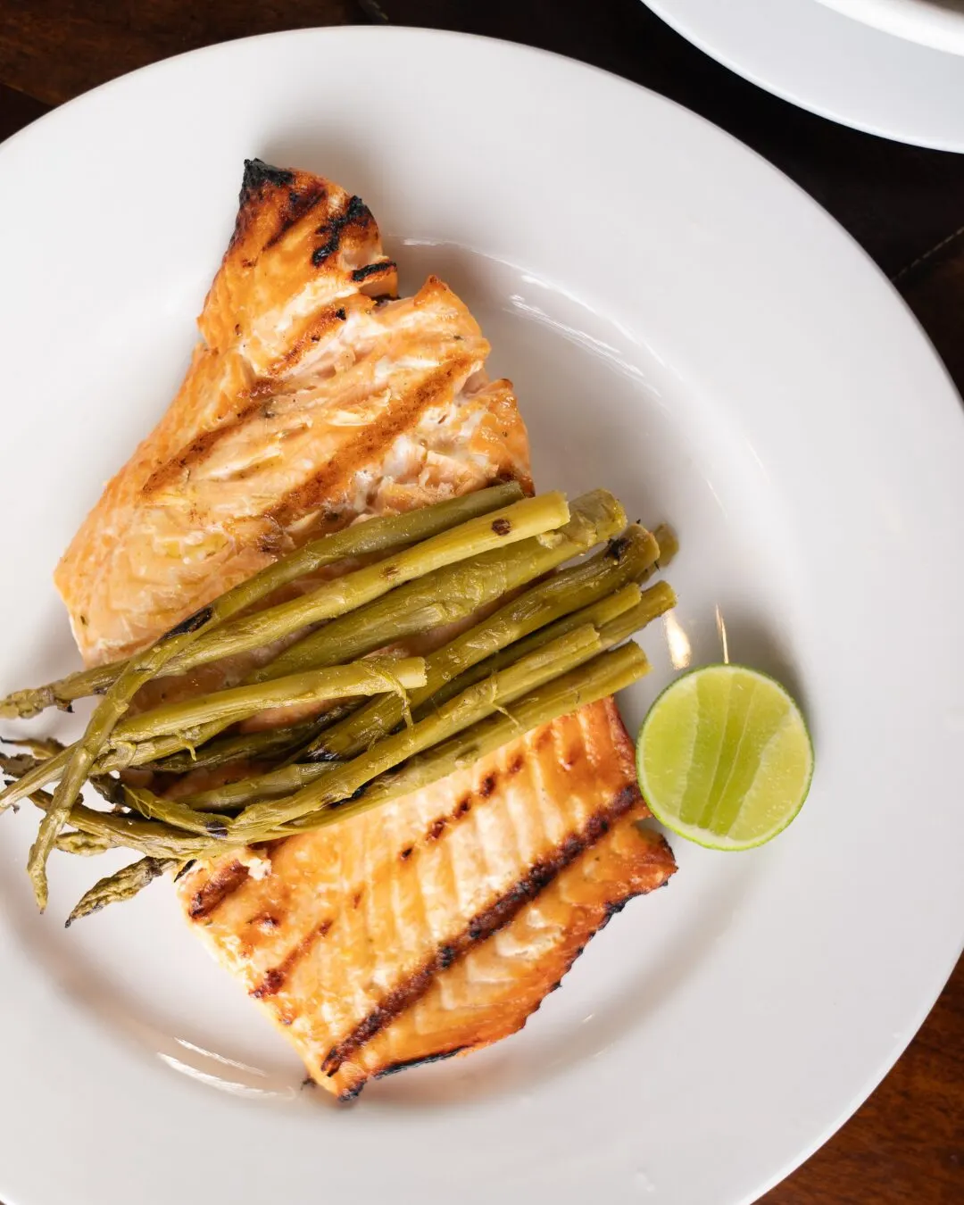 Pescado a la parrilla con espárragos y una rodaja de limón.
