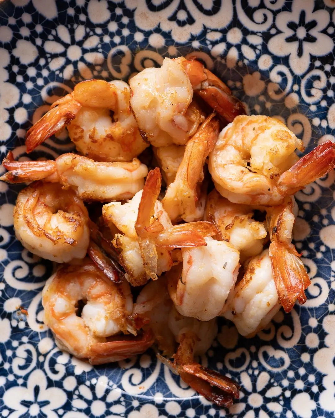 Camarones salteados sobre un plato azul y blanco estampado.
