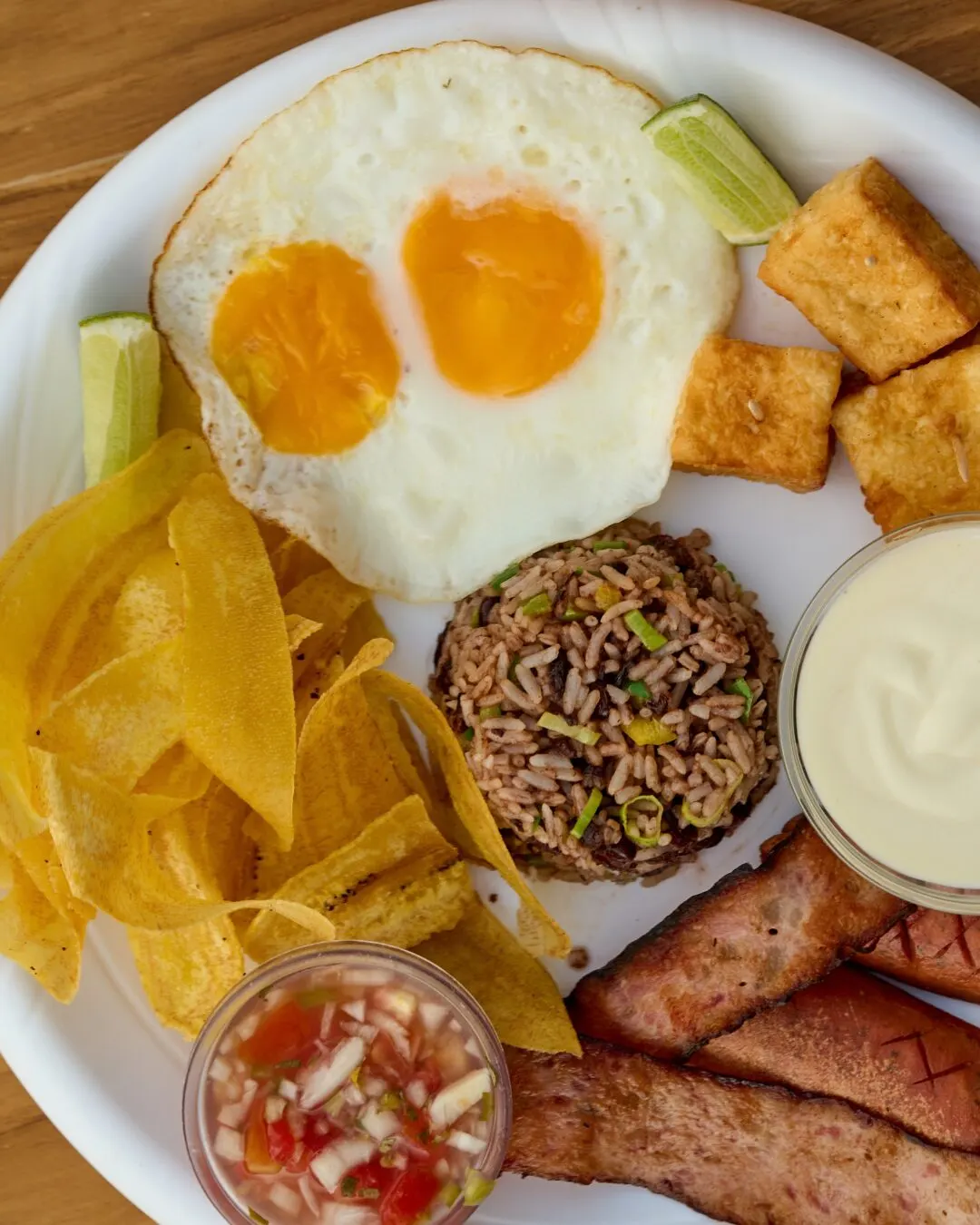 Breakfast with fried eggs, fried plantain, gallo pinto (rice and beans), sausage and cream on a white plate.