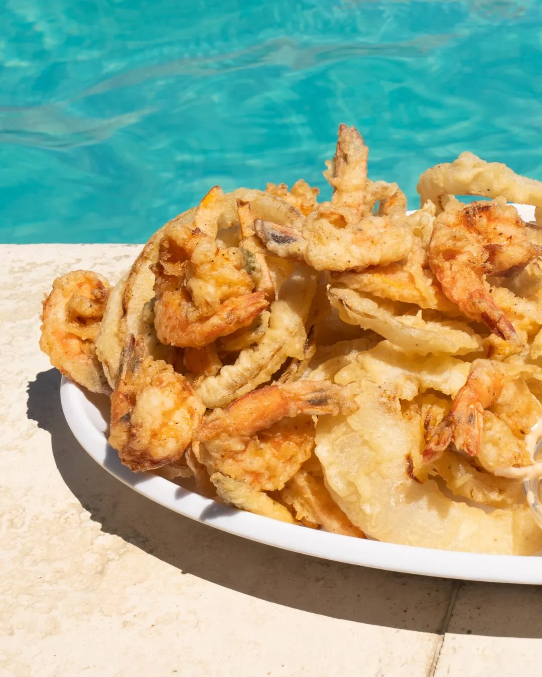 A plate of fried shrimp at the pool's edge, with turquoise water behind.