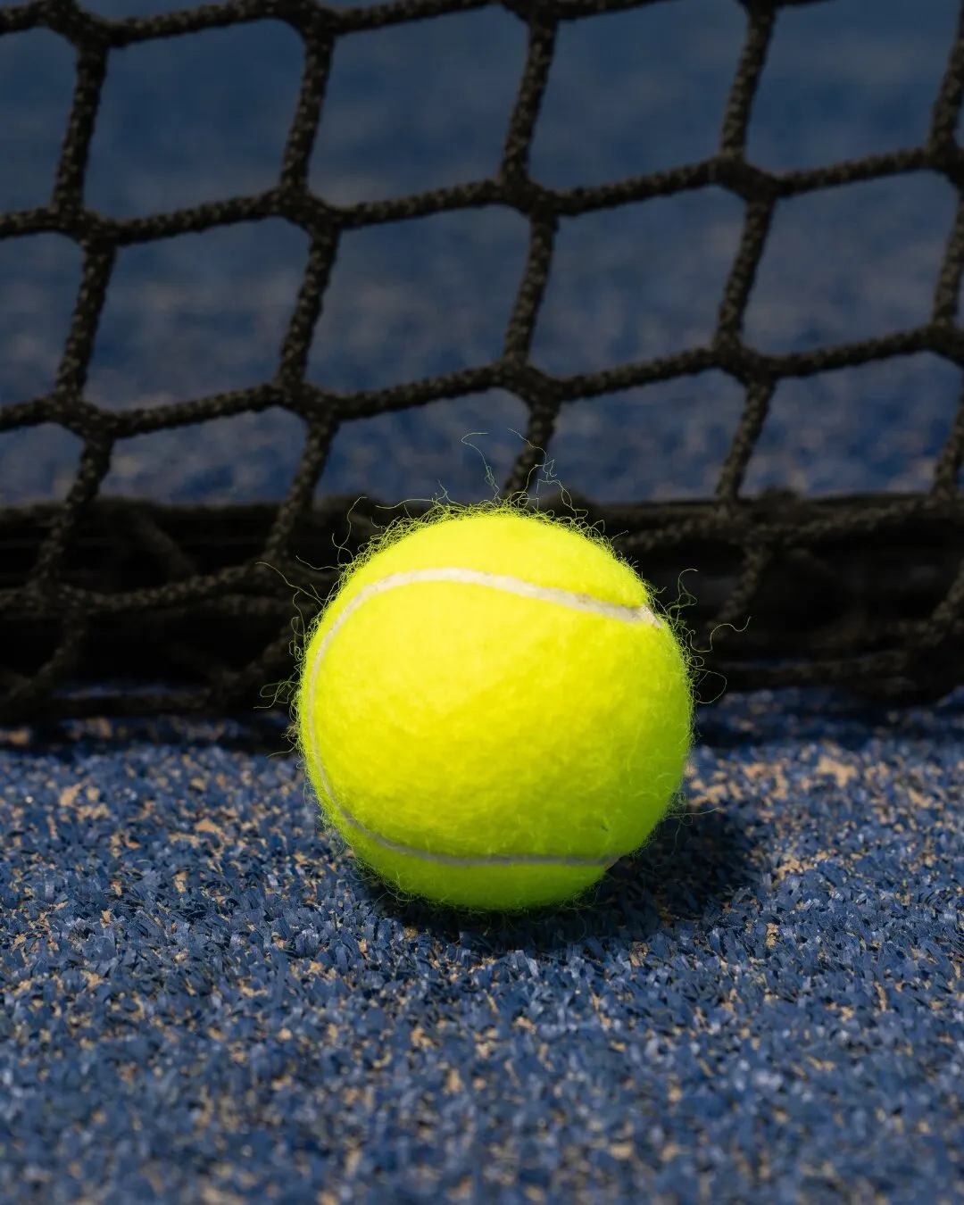Pelota amarilla sobre la superficie azul de la cancha, junto a la red.