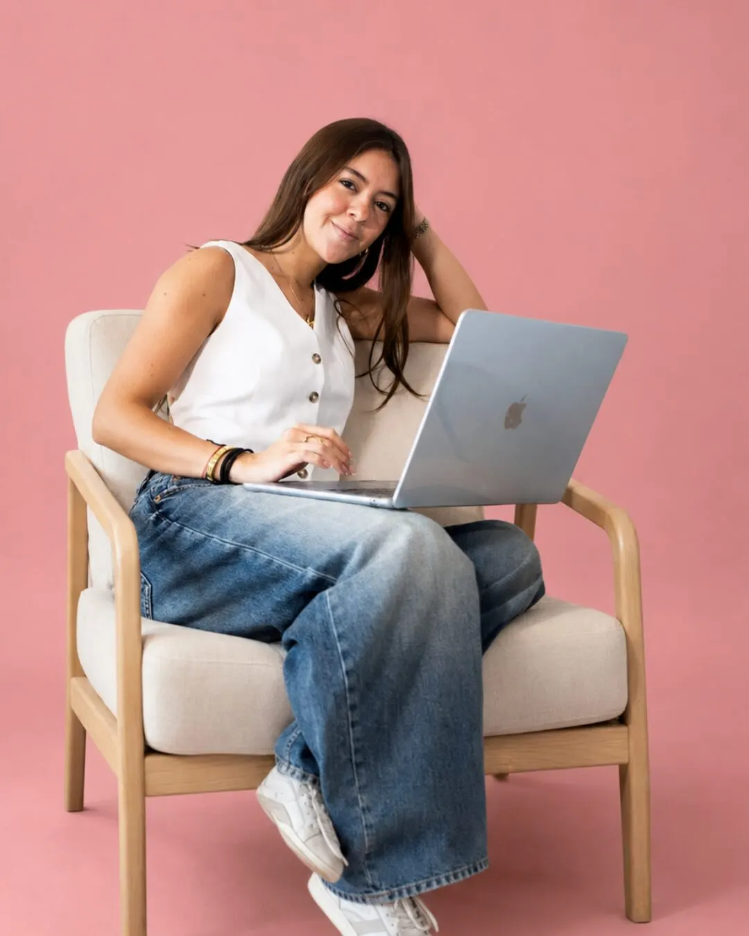 Una integrante del equipo de Social Hour sentada con una laptop sobre un fondo rosa